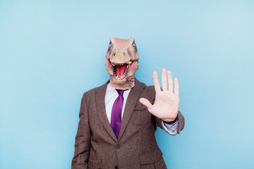 Euphoric man with lizard head showing hand in stop sign on blue background.