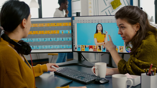 Photographers using professional retouching software or application to edit photos with stylus pen, discussing in front of computer with dual monitors setup. Project managet pointing on display.