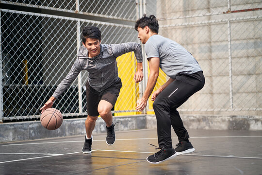 Two Young Asian Men Playing Basketball Outdoors