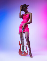 a dark-skinned woman in a pink short dress and a hat with an electric guitar