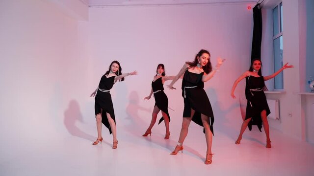 A dancing aerobic class of a women's modern dances. A group of girls are dancing in the studio in black dresses.