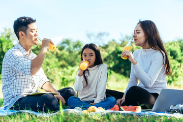 happy Asian family is having picnic in garden and drinking Orange juice in bottle with their daughters on holiday happily.