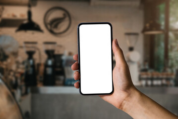 Hand holding white mobile phone with blank white screen in cafe.