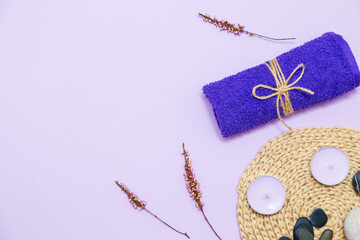 Scented candles, towel, lotion and pebbles on a lilac background.
