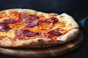 Delicious homemade pizza on a wooden plate against the black background