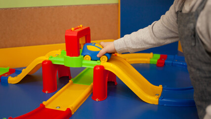 A two-year-old girl plays with toys in the playroom. Development Centre, Kindergarten Baby plays with plastic typewriter, road designer, multi-colored race track the car rolls on the road