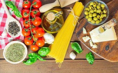 Italian food background, with vine tomatoes, oregano, basil, spaghetti, olives, parmesan, olive oil, garlic, peppercorns. wood background.  concept food.