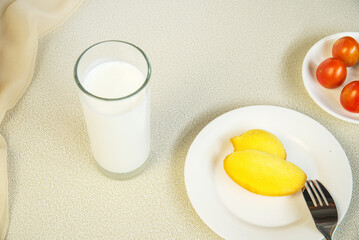 Golden bread on a white plate with a cup of milk, tomatoes, a fork, nutritious breakfast, top view