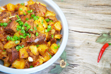 On a natural wooden board, there is a plate of braised pork with potatoes and spring onions, a traditional Chinese delicious diet