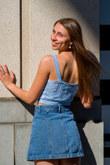 Smiling teenage girl with back to camera standing against a wall in an downtown area