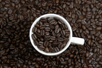 A cup of coffee beans on the background covered with coffee beans, top view