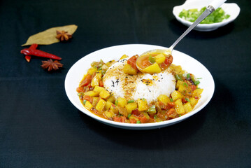 Stir-fried potato and green pepper on rice, a spoon, black background