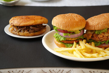 Close-up three hamburgers, chicken, steak, french fries, black background