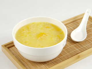 Pumpkin millet porridge and a spoon on bamboo roller mat on wooden board, white background