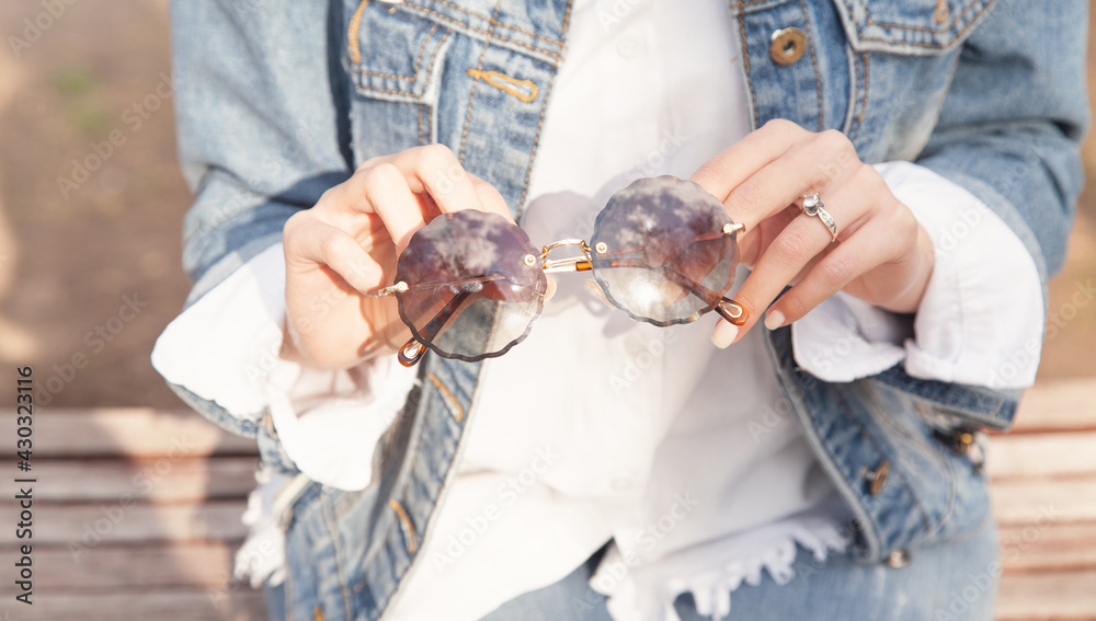 Wall mural Young woman holding sunglasses in outdoors.