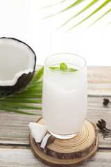 A glass of coconut juice and coconut shell on a wooden round board, healthy nutritious drink