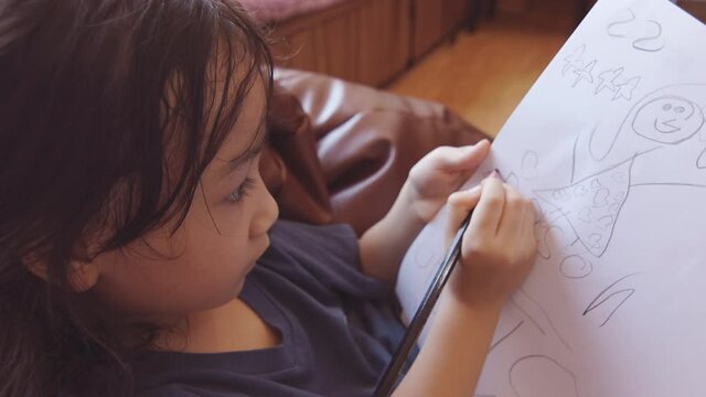 Face focusing 4K clip of asian adorable girl sitting on bead sofa and writing on paper which is learning at home shows alternative education. She sit near window with warm tone light of sunrise.