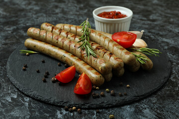 Tray with grilled sausage, spices and sauce on black smokey background