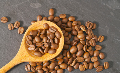 Coffee beans in wooden spoon placed on black marble background