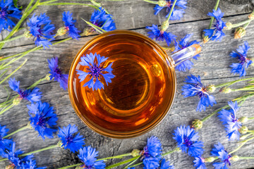 Obraz na płótnie Canvas Cup of herbal tea and blue cornflowers flowers on wood background. Top view Flat lay Copy space.