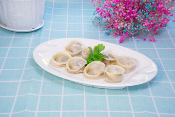 Yuanbao dumplings on a white plate on blue checkered tablecloth, with purple flowers set off
