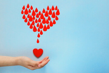 baby's hand catch blood drops and heart on blue background, world blood donor day, charity and...