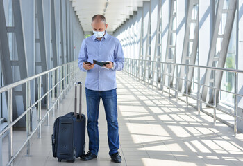 Fototapeta na wymiar Man in a medical mask with tickets, passport, with a suitcase at the airport or shopping mall. Safe travel during the coronavirus outbreak. Lockdown, Quarantine.Safe Business travel