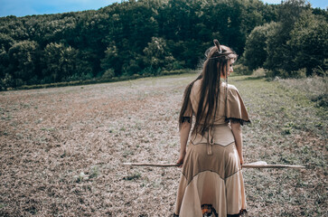 Young native american woman with a spear walking to the forest, indian cosplay, tribal warrior...