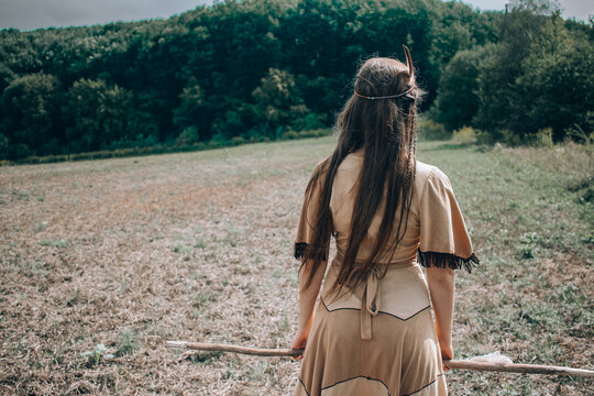 Young native american woman with a spear walking to the forest, indian cosplay, tribal warrior concept, beautiful young girl in indian tribe costume posing with back turned to camera