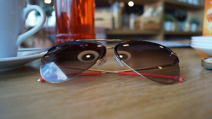 the tinted glasses lie on the wooden table next to a white mug. in the glasses, the reflection of...