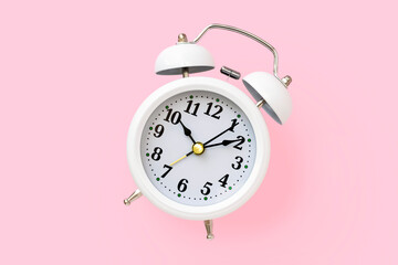White metal retro alarm clock with a round dial on a pink background, top view. Minimalistic...