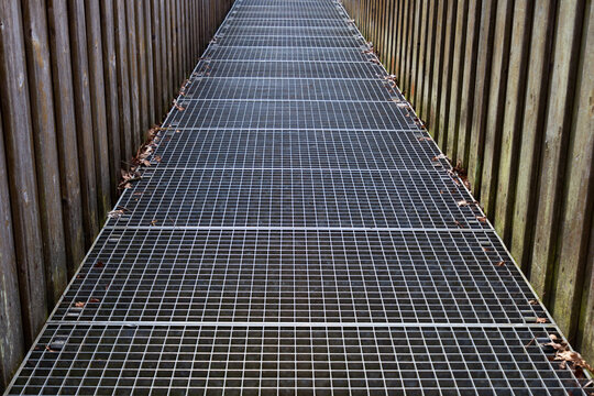 Footbridge with iron grating floor and wooden railing crossing a river