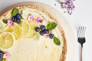cheesecake with lemon and blueberries decorated with flowers on a wooden base on a light background top view