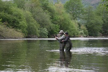 fishing guide with a young woman fly fishing for trout in a clear river