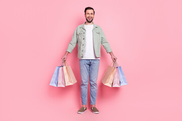 Full length body size view of attractive cheerful guy holding in hands bags gifts isolated over pink pastel color background