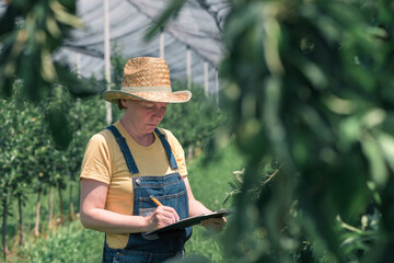 Female farmer writing production notes in apple fruit orchard