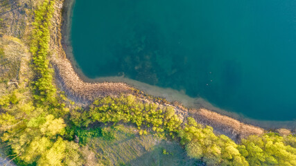 Aerial view of a picturesque place where transparent turquoise water of a forest lake meets a stony shore with trees in spring. captured with a drone. High quality photo