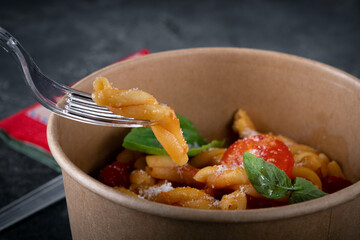 Casarecce pasta with tomato and basil in a taking away box. food delivery from the restaurant to your home. Close up, selective focus
