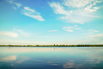 A quiet lake against a blue sky with clouds and forest