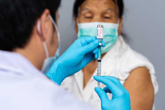 doctor draws medication out of vial before injection with syringe to senior patient and wearing medical mask. Covid-19 or coronavirus vaccine