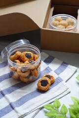a jar of thumbprint cookies with jam and grated cheese in white background