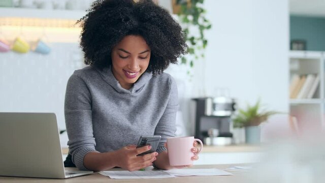 Video of beautiful afro business woman talking with her mobile phone while working with computer in the kitchen at home.