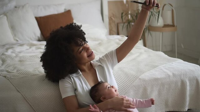 Mom taking selfie photo with baby girl and sitting in bright home bedroom spbd.