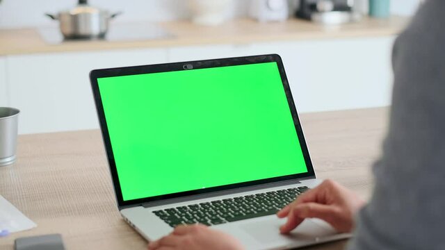 Video of afro business woman using laptop computer with a green screen on monitor in the kitchen at home.