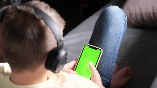 Boy lying on couch using smartphone with chroma key green screen, scrolling through  internet, play game or study. Home interior