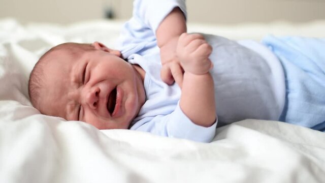 Little baby newborn crying, cry scream, cries loudly. New born child tired and hungry in bed on white blanket. Infant screaming. Healthy little kid shortly after birth. Portrait. Infancy, babyhood