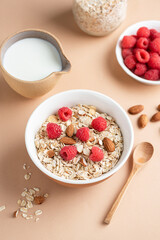 Oat muesli with almonds and raspberries in a bowl. Healthy breakfast food, clean eating, dieting concept. Beige background