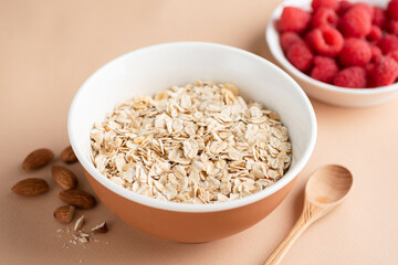 Oat flakes in bowl ready for cooking oatmeal porridge. Oat muesli on beige background. Healthy breakfast cereals food, dieting, fitness food menu concept