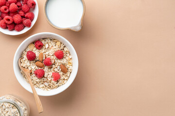 Fototapeta na wymiar Uncooked dry oats muesli with nuts and berries in bowl and almond milk in jug on beige background, top view, copy space