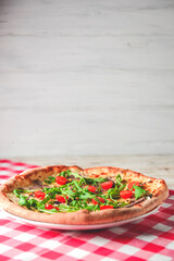 Prosciutto and Arugula Pizza with cherry tomatoes served on a white plate over red plaid table cloth.